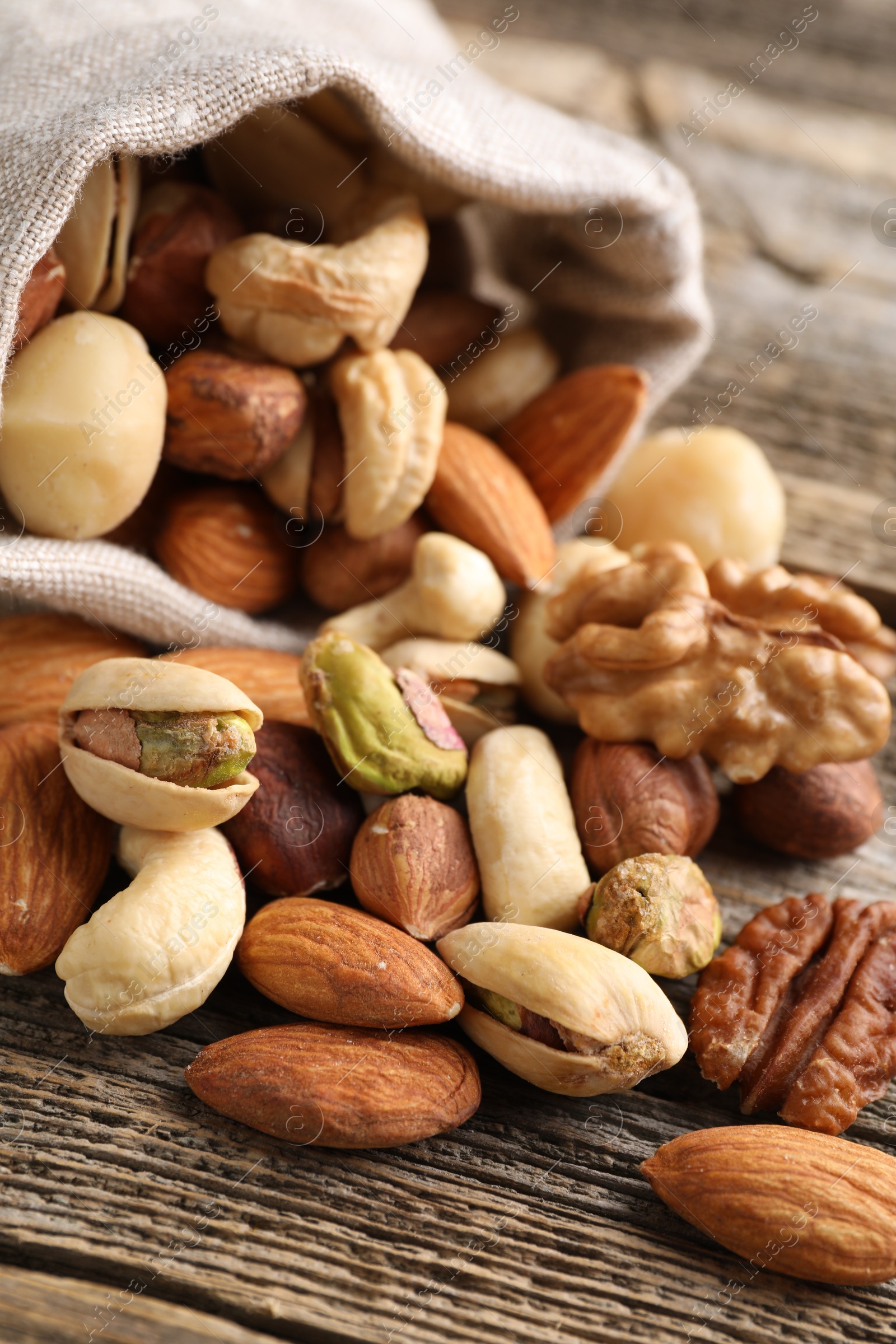 Photo of Mix of different nuts in bag on wooden table, closeup