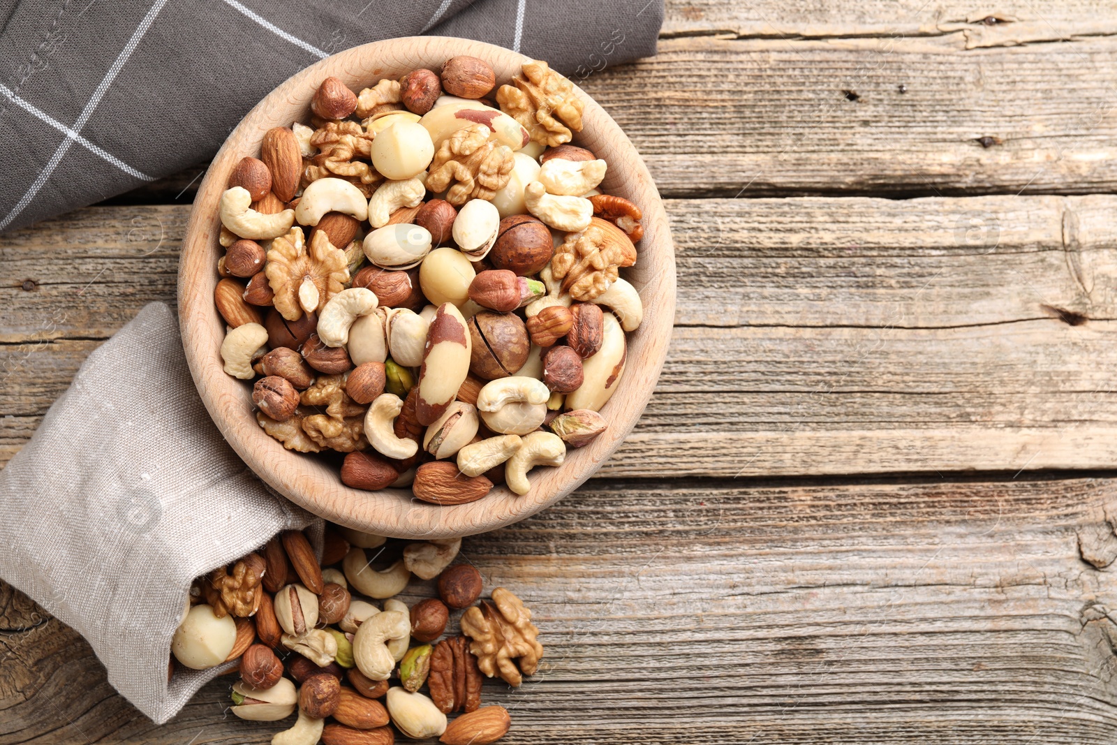 Photo of Mix of different nuts in bowl and bag on wooden table, top view. Space for text