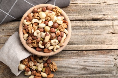 Photo of Mix of different nuts in bowl and bag on wooden table, top view. Space for text