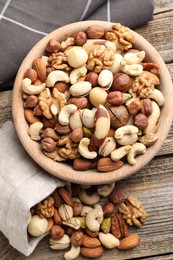 Photo of Mix of different nuts in bowl and bag on wooden table, top view