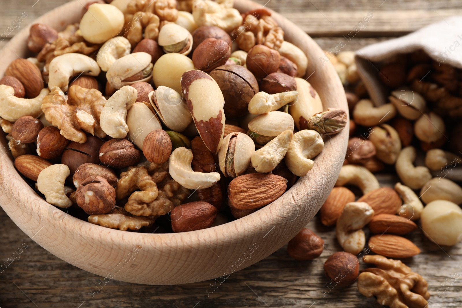 Photo of Mix of different nuts in bowl and bag on wooden table, closeup