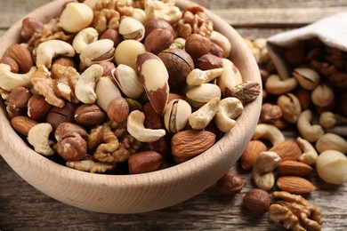 Photo of Mix of different nuts in bowl and bag on wooden table, closeup