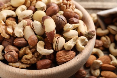Photo of Mix of different nuts in bowl on wooden table, closeup