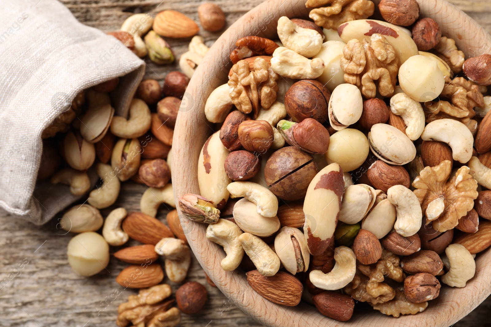 Photo of Mix of different nuts in bowl and bag on wooden table, top view