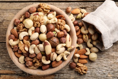 Photo of Mix of different nuts in bowl and bag on wooden table, top view