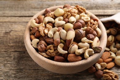 Photo of Mix of different nuts in bowl on wooden table, closeup