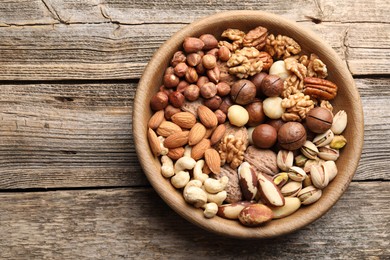 Photo of Mix of different nuts in bowl on wooden table, top view. Space for text
