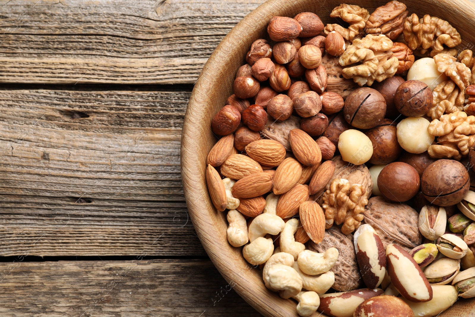 Photo of Mix of different nuts in bowl on wooden table, top view. Space for text