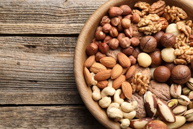 Photo of Mix of different nuts in bowl on wooden table, top view. Space for text