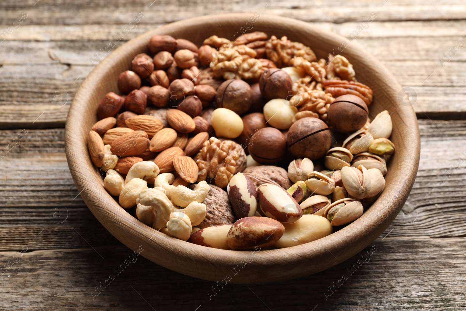 Photo of Mix of different nuts in bowl on wooden table, closeup