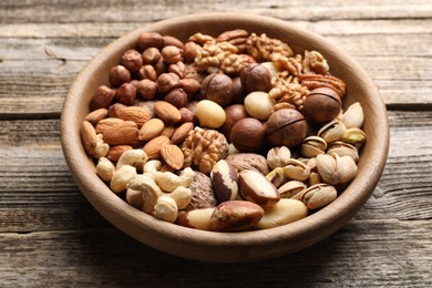 Photo of Mix of different nuts in bowl on wooden table, closeup