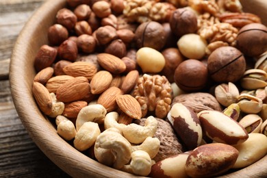 Photo of Mix of different nuts in bowl on wooden table, closeup