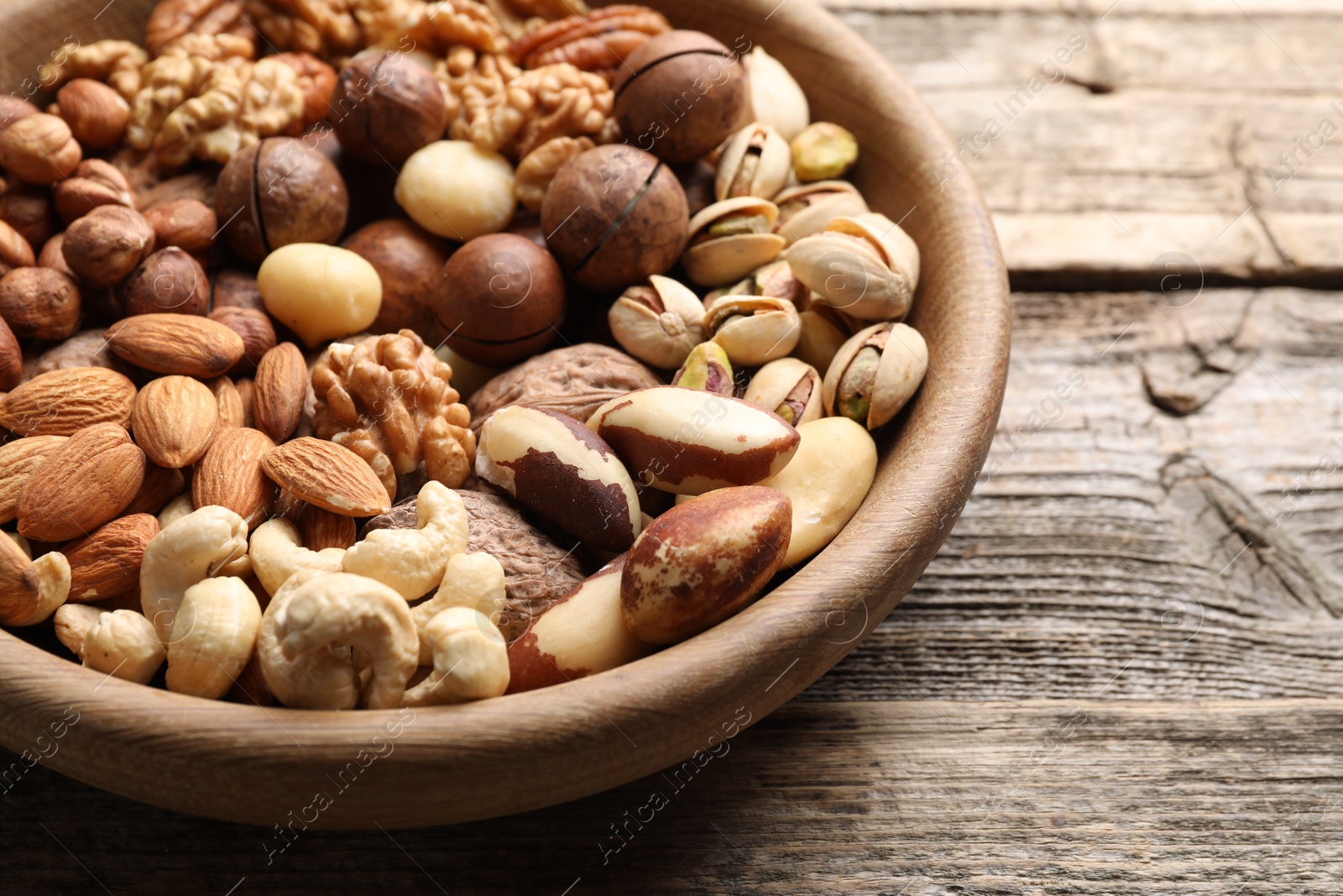 Photo of Mix of different nuts in bowl on wooden table, closeup
