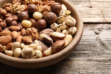 Photo of Mix of different nuts in bowl on wooden table, closeup