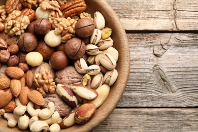Photo of Mix of different nuts in bowl on wooden table, top view. Space for text