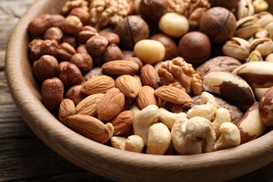 Photo of Mix of different nuts in bowl on wooden table, closeup