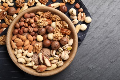 Photo of Mix of different nuts in bowl on black table, top view. Space for text