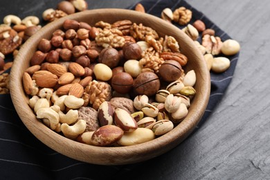 Photo of Mix of different nuts in bowl on black table, closeup