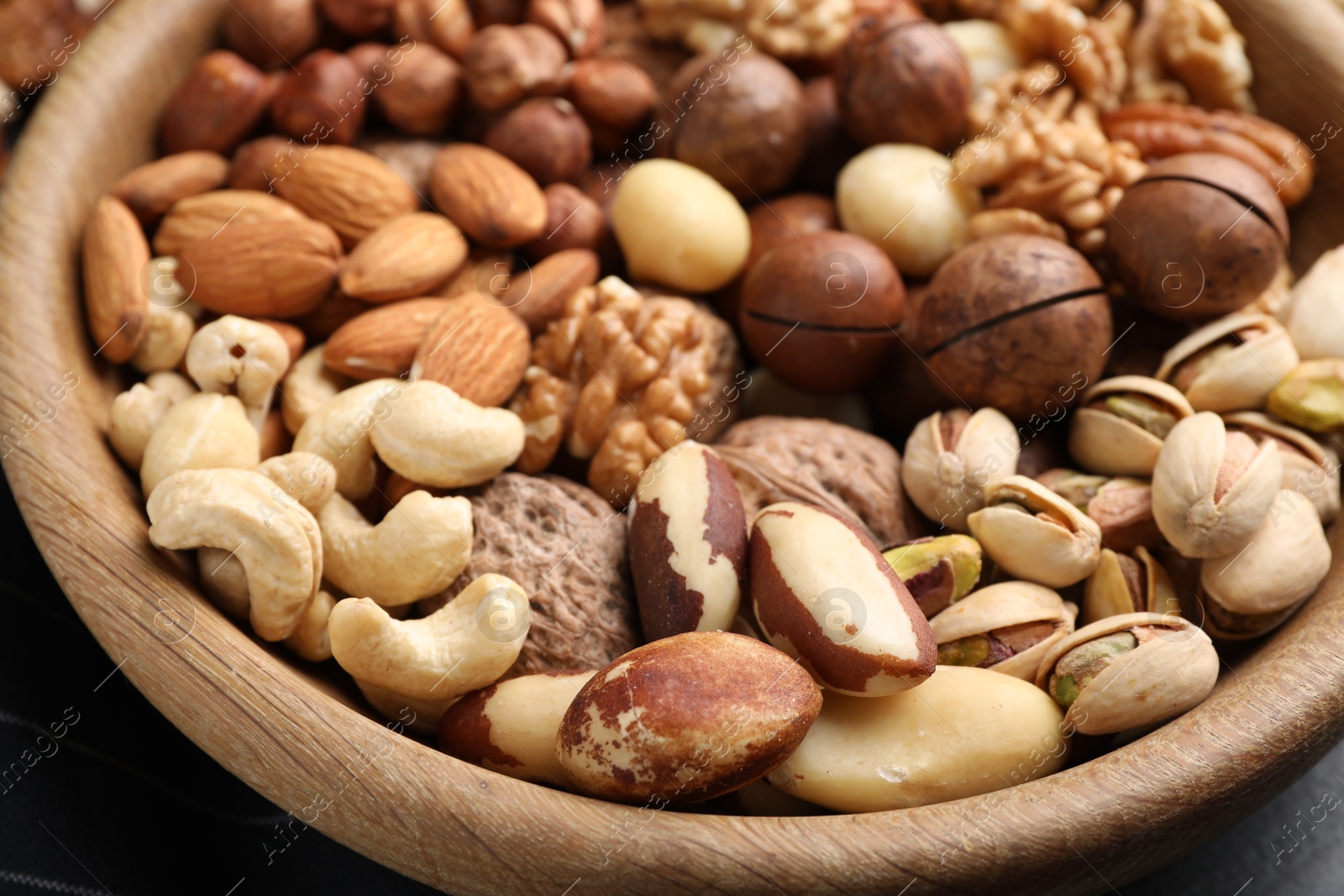 Photo of Mix of different nuts in bowl on black table, closeup