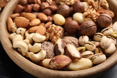 Photo of Mix of different nuts in bowl on black table, closeup