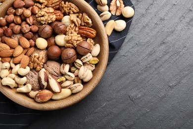 Photo of Mix of different nuts in bowl on black table, top view. Space for text