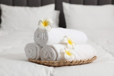 Photo of Rolled white towels and plumeria flowers on bed, closeup