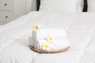 Photo of Rolled white towels and plumeria flowers on bed indoors