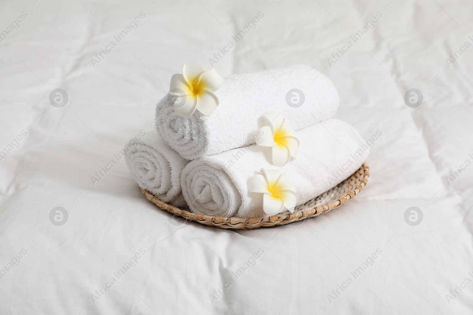 Photo of Rolled white towels and plumeria flowers on bed linens, closeup