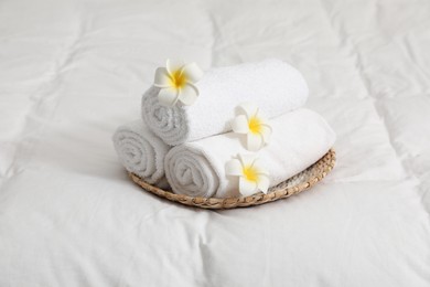 Photo of Rolled white towels and plumeria flowers on bed linens, closeup