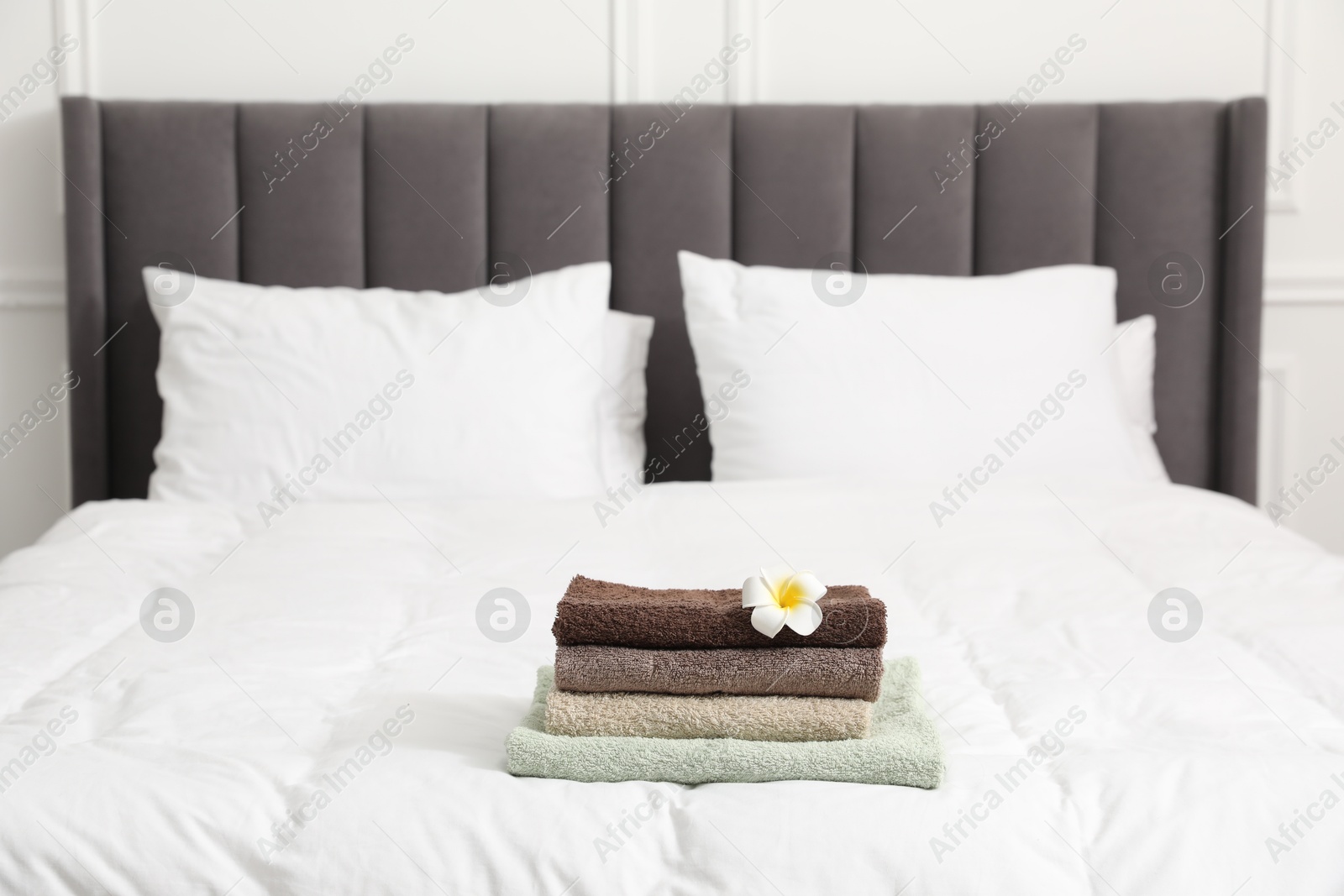 Photo of Stack of terry towels and plumeria flower on bed indoors