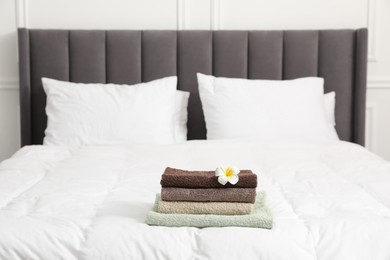Photo of Stack of terry towels and plumeria flower on bed indoors
