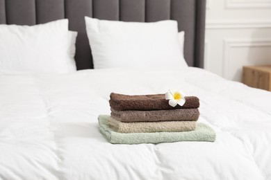 Photo of Stack of terry towels and plumeria flower on bed indoors