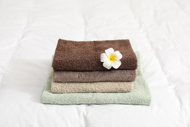Photo of Stack of terry towels and plumeria flower on bed linens, closeup
