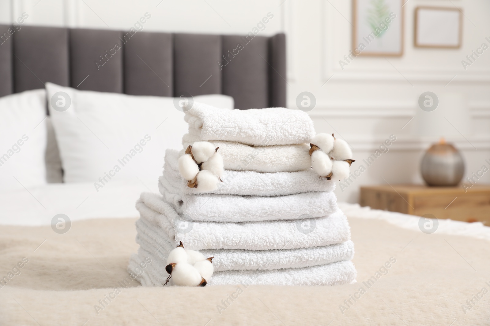 Photo of Stack of white terry towels and cotton flowers on bed indoors