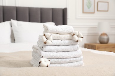 Photo of Stack of white terry towels and cotton flowers on bed indoors