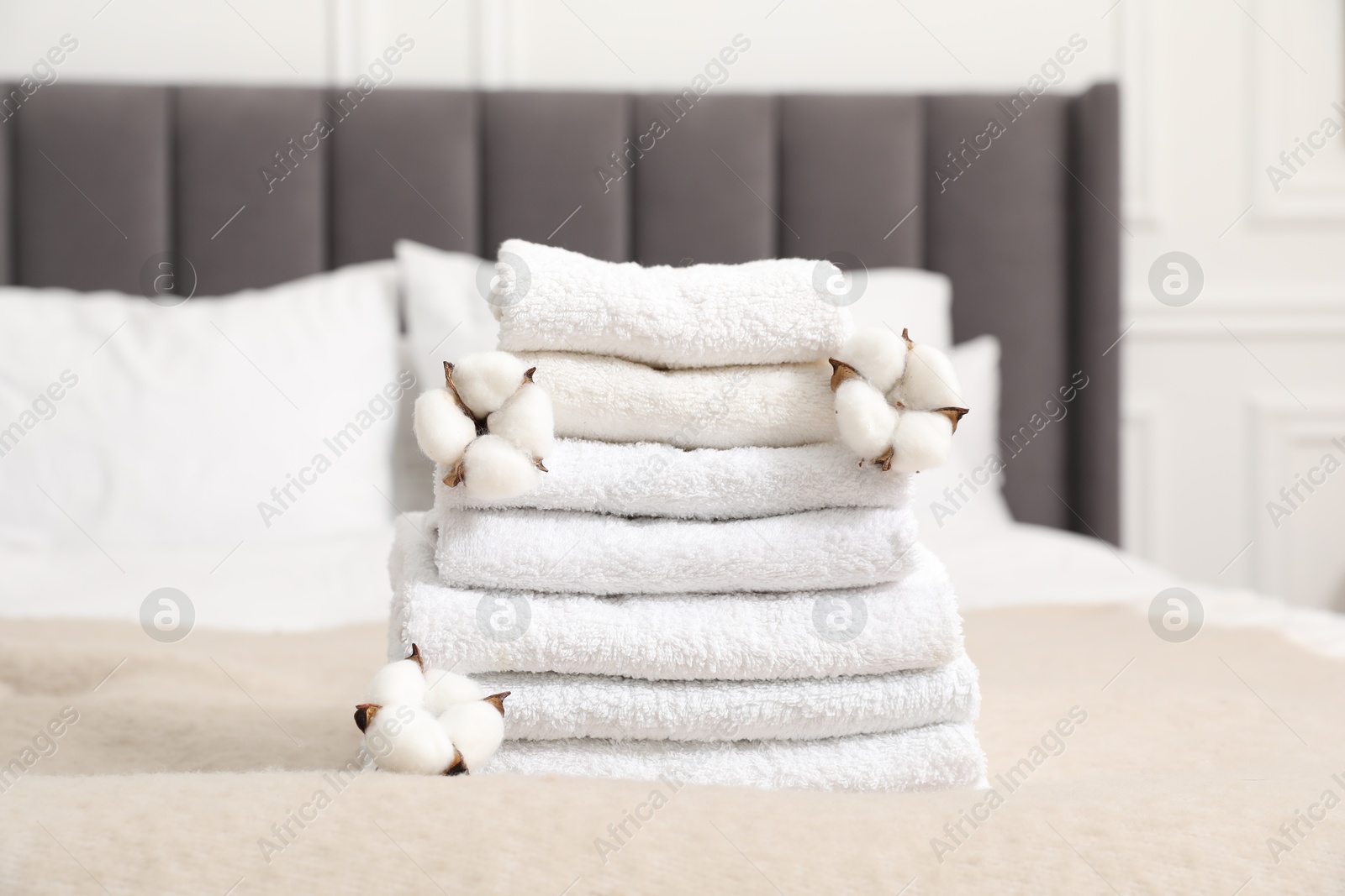 Photo of Stack of white terry towels and cotton flowers on bed indoors