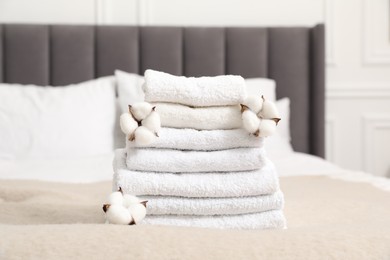 Photo of Stack of white terry towels and cotton flowers on bed indoors