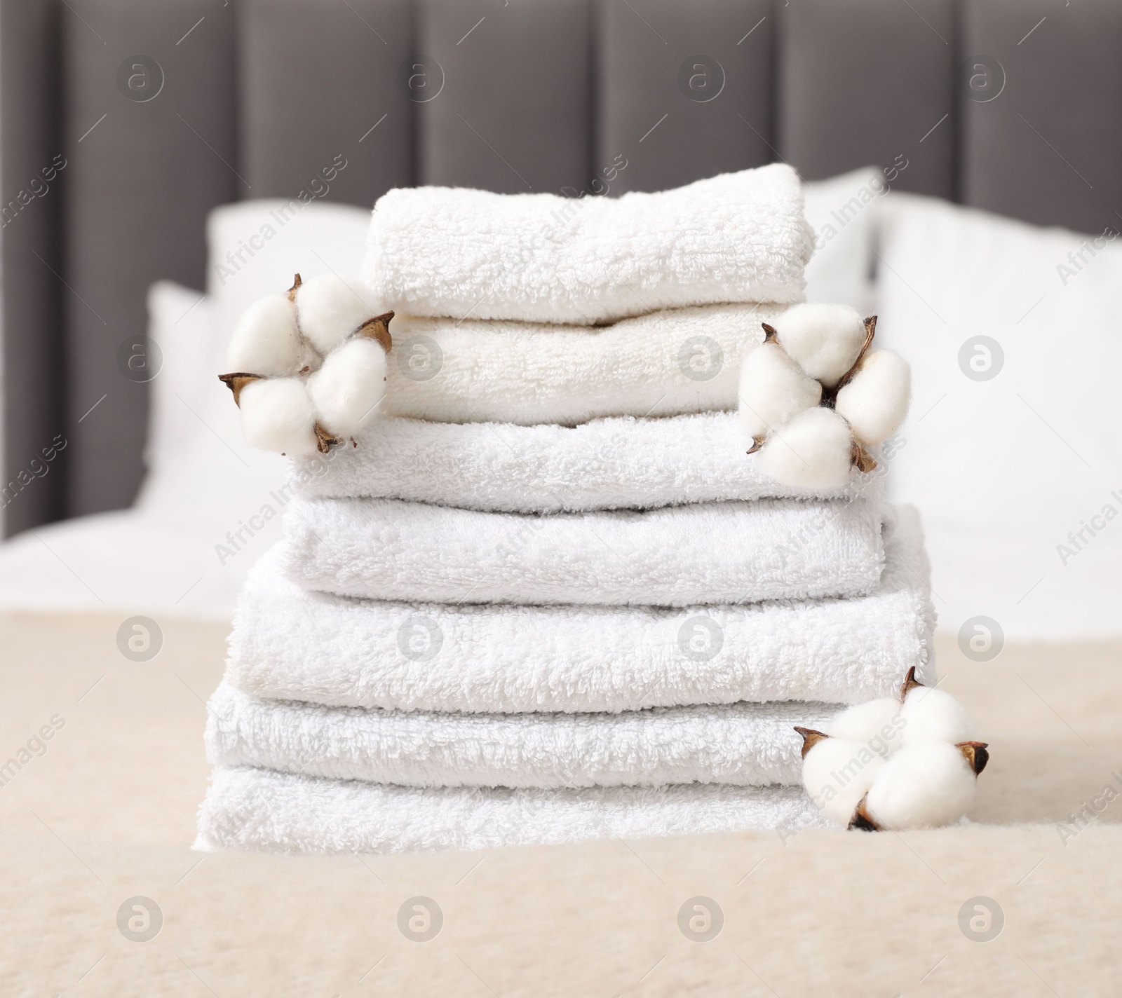 Photo of Stack of white terry towels and cotton flowers on bed indoors, closeup