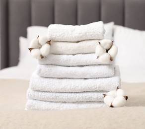 Photo of Stack of white terry towels and cotton flowers on bed indoors, closeup