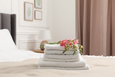 Photo of Stack of white terry towels and beautiful flowers on bed indoors
