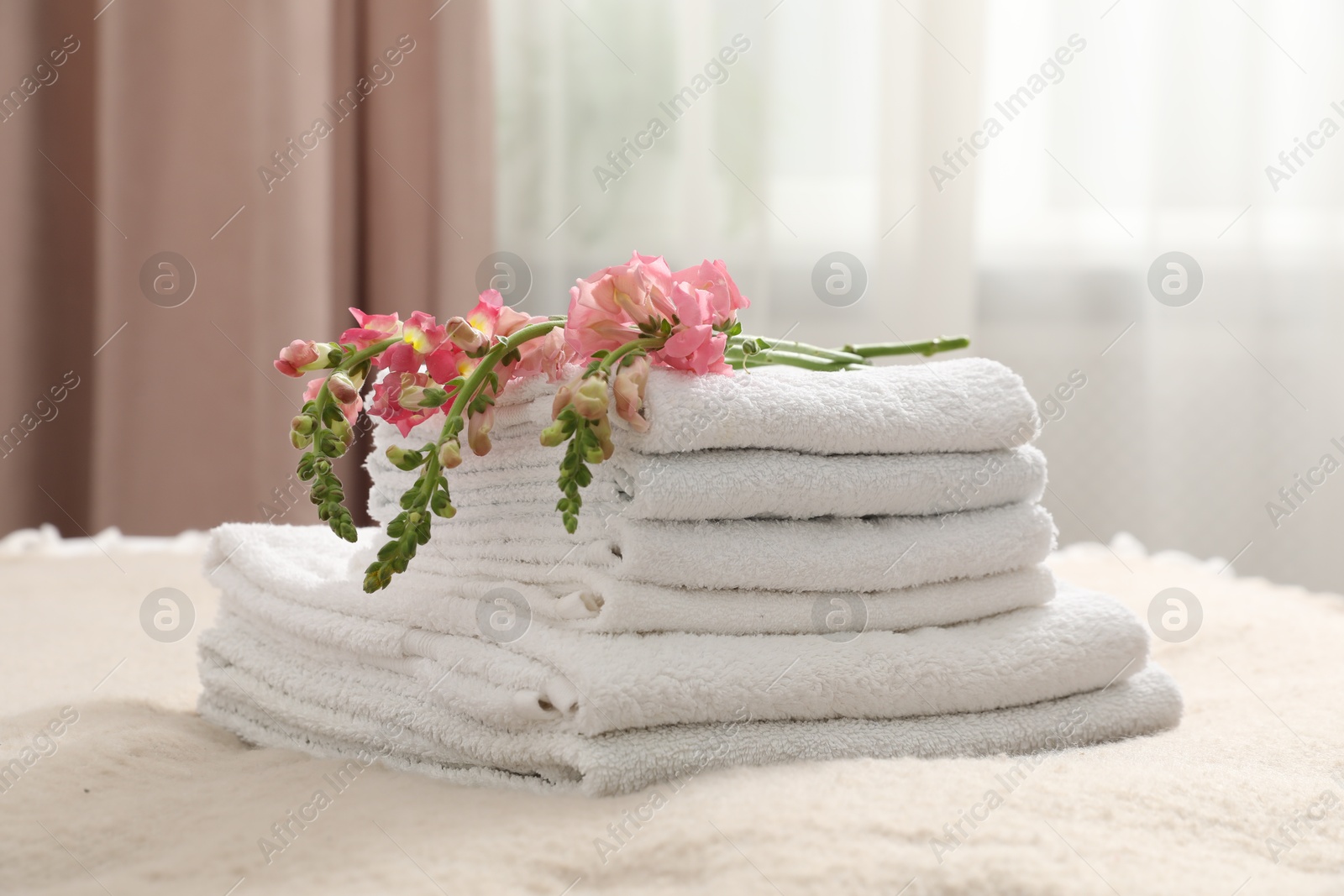 Photo of Stack of white terry towels and beautiful flowers on bed indoors, closeup