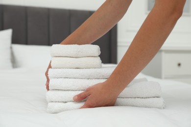 Photo of Woman putting stack of white terry towels onto bed indoors, closeup