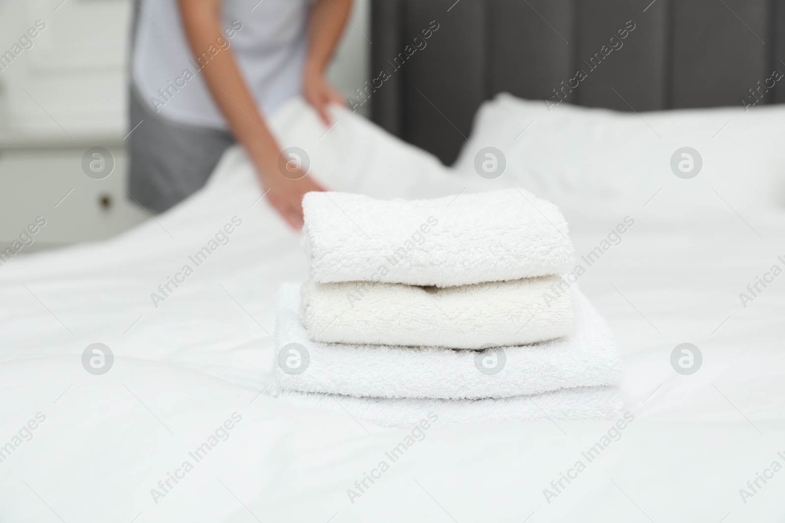 Photo of Chambermaid working in hotel room, focus on stack of terry towels on bed