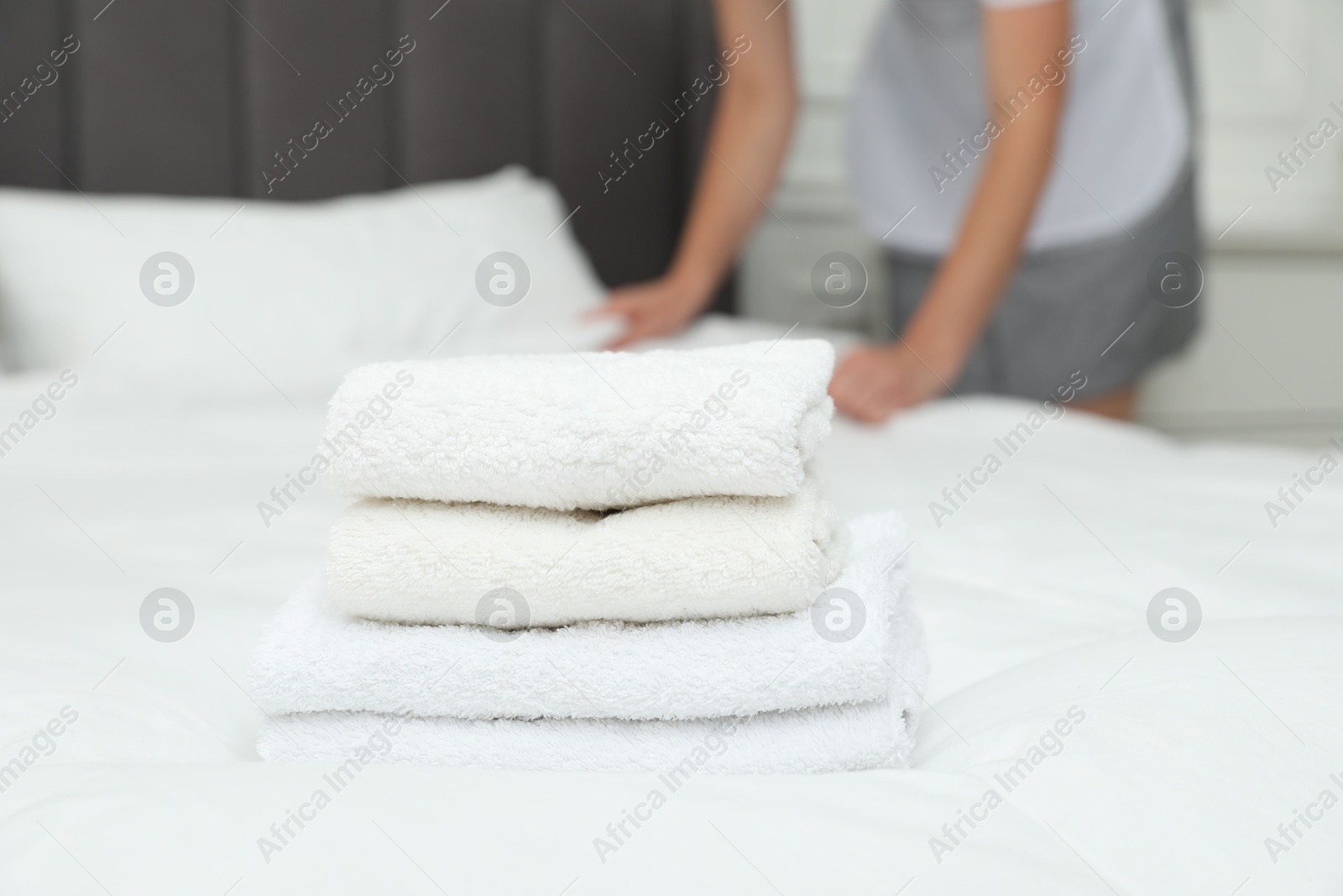 Photo of Chambermaid working in hotel room, focus on stack of terry towels on bed