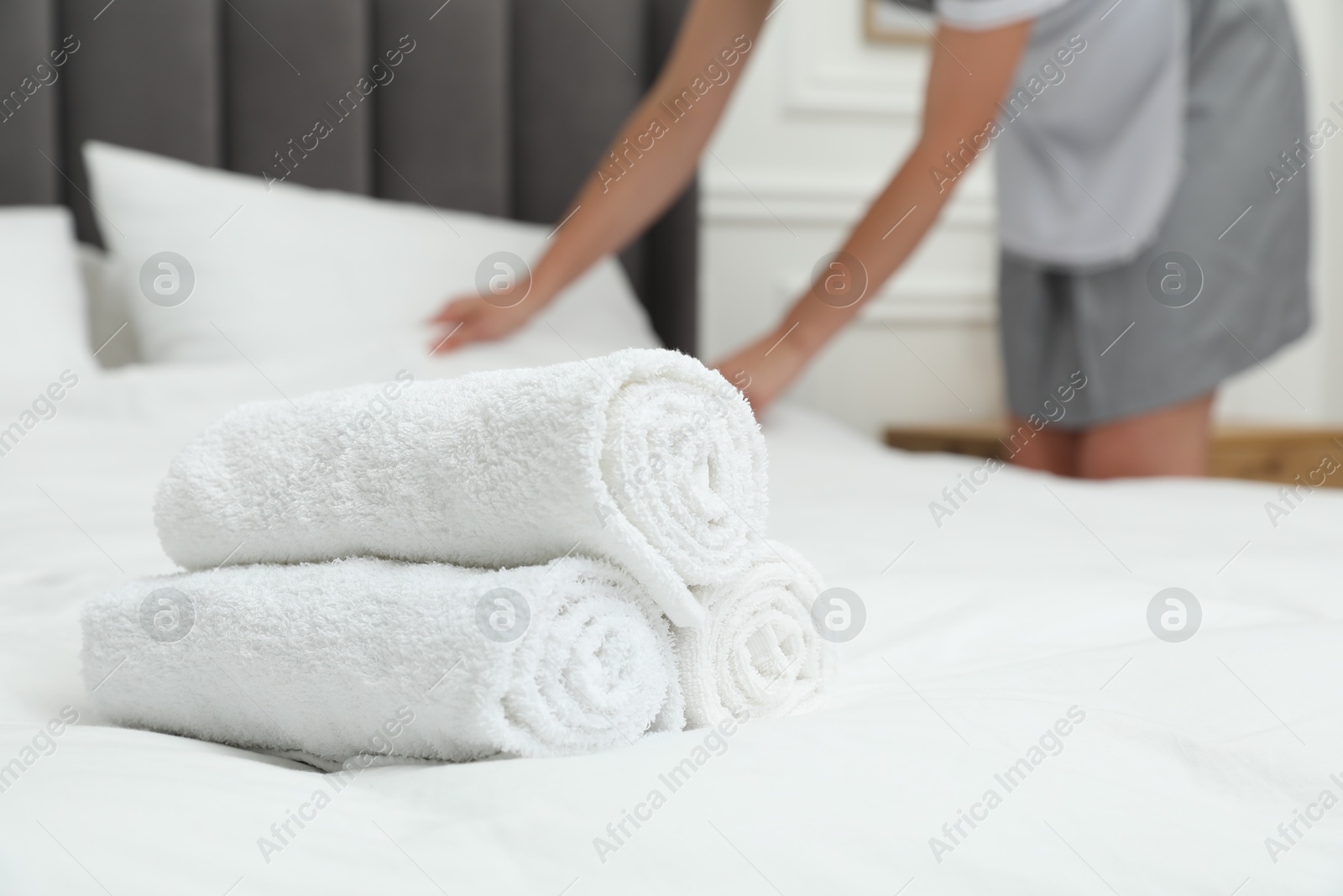 Photo of Chambermaid working in hotel room, focus on stack of terry towels on bed