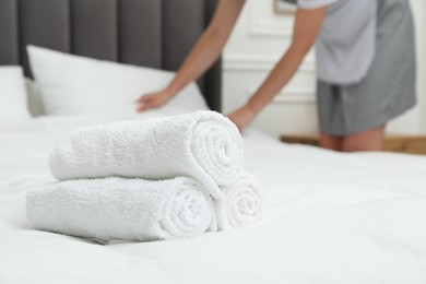 Photo of Chambermaid working in hotel room, focus on stack of terry towels on bed