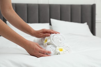 Photo of Woman putting stack of white terry towels and plumeria flowers onto bed indoors, closeup