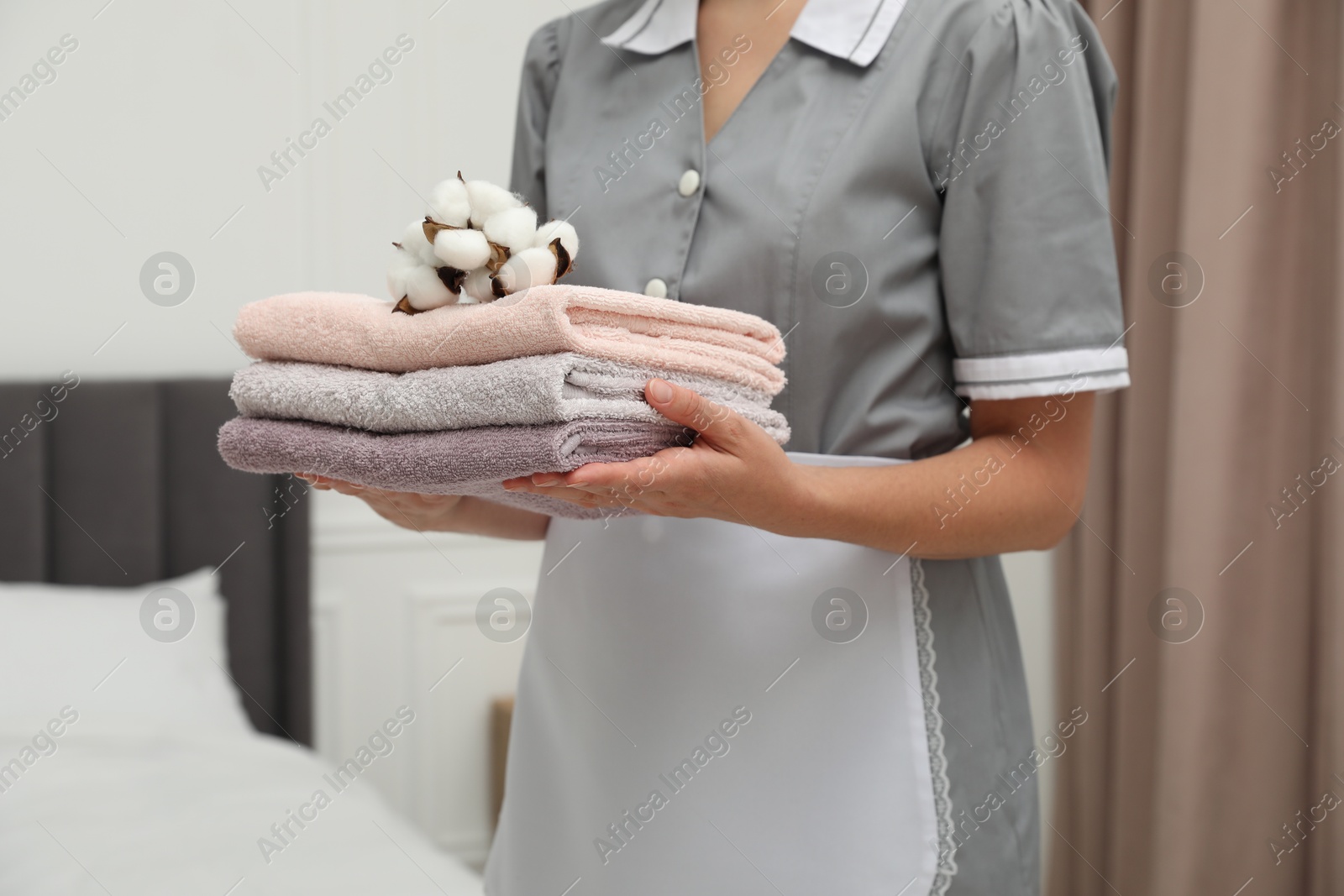 Photo of Chambermaid with stack of terry towels and cotton flowers in hotel room, closeup