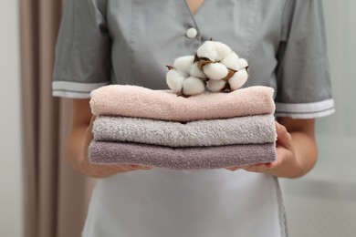 Photo of Chambermaid with stack of terry towels and cotton flowers in hotel room, closeup