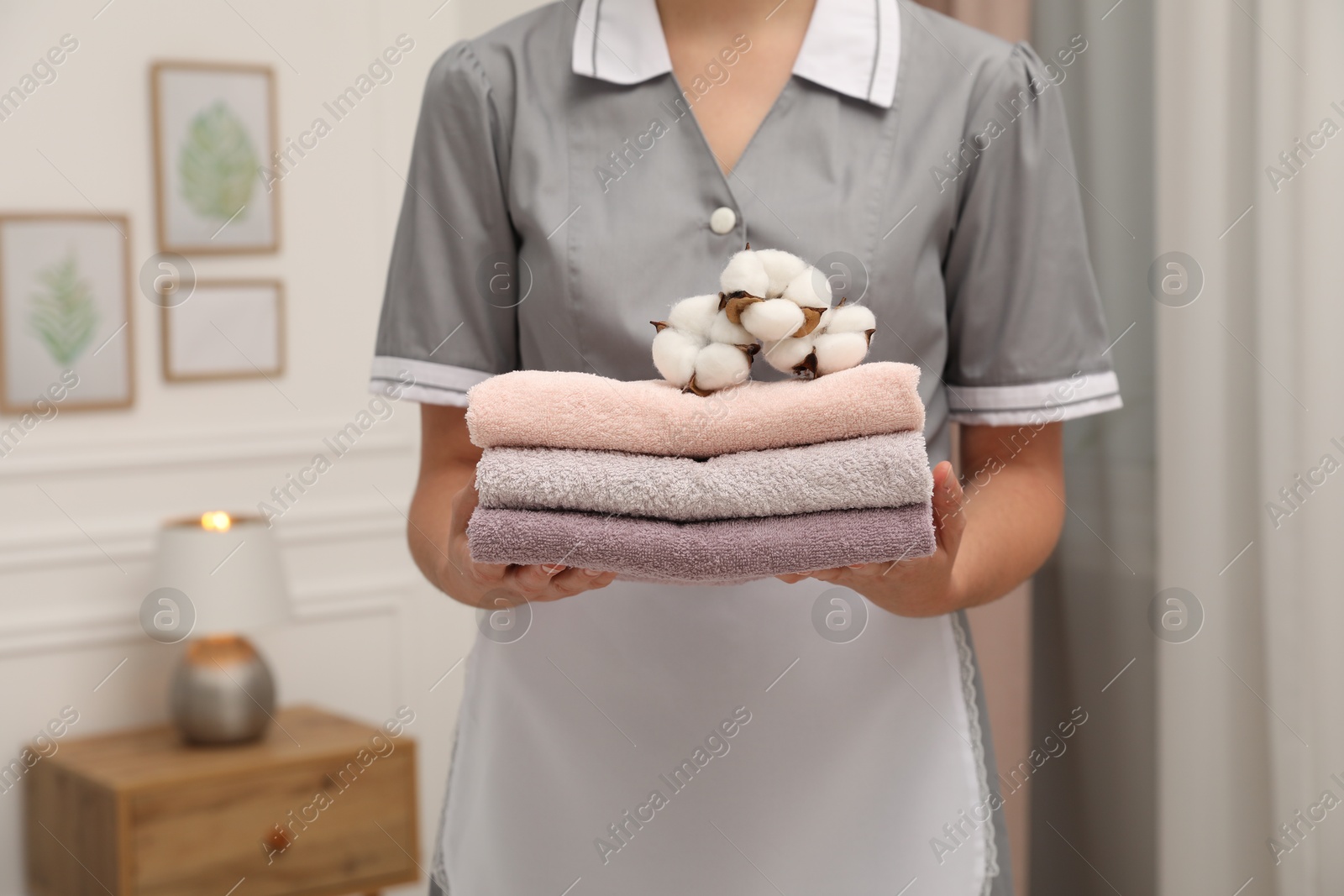 Photo of Chambermaid with stack of terry towels and cotton flowers in hotel room, closeup